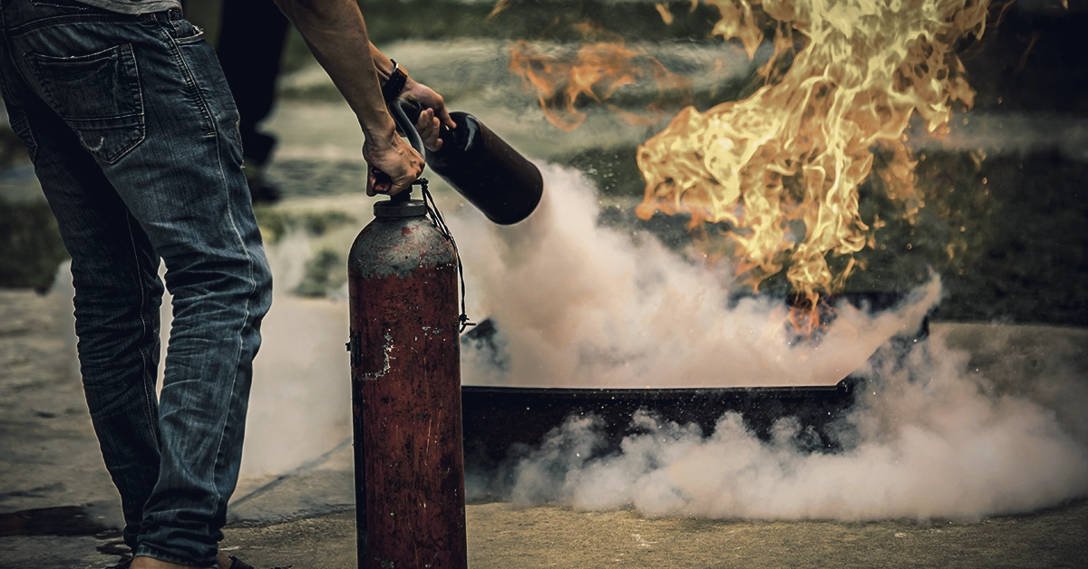 Homem acionando extintor de incêndio vermelho contra chamas, representando a segurança em espaços religiosos como terreiros, representando a capa do artigo Guia Completo para Segurança e Inclusão nos Terreiros: Um Compromisso com o Axé Vivo