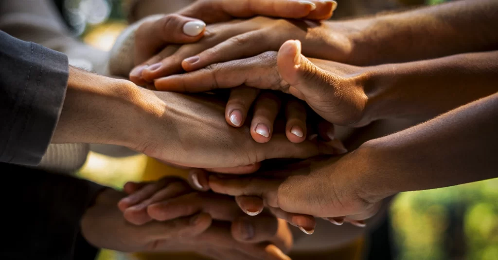 Mãos diversas empilhadas simbolizando união e responsabilidade coletiva em Ilês de Axé