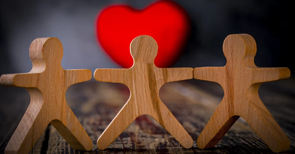 Bonecos de madeira de mãos dadas com coração ao fundo simbolizando solidariedade e cuidado legal
