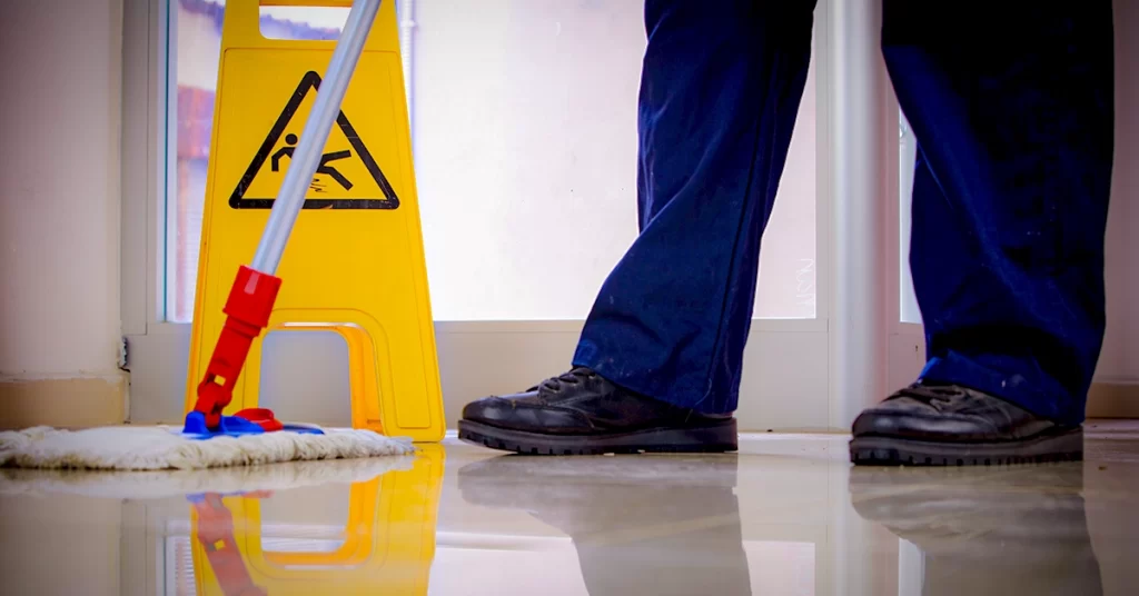 Sinal de piso molhado amarelo com balde e rodo, perto de pés calçados
