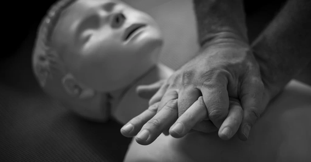 Mãos realizando compressões torácicas em manequim de RCP, simulando primeiros socorros