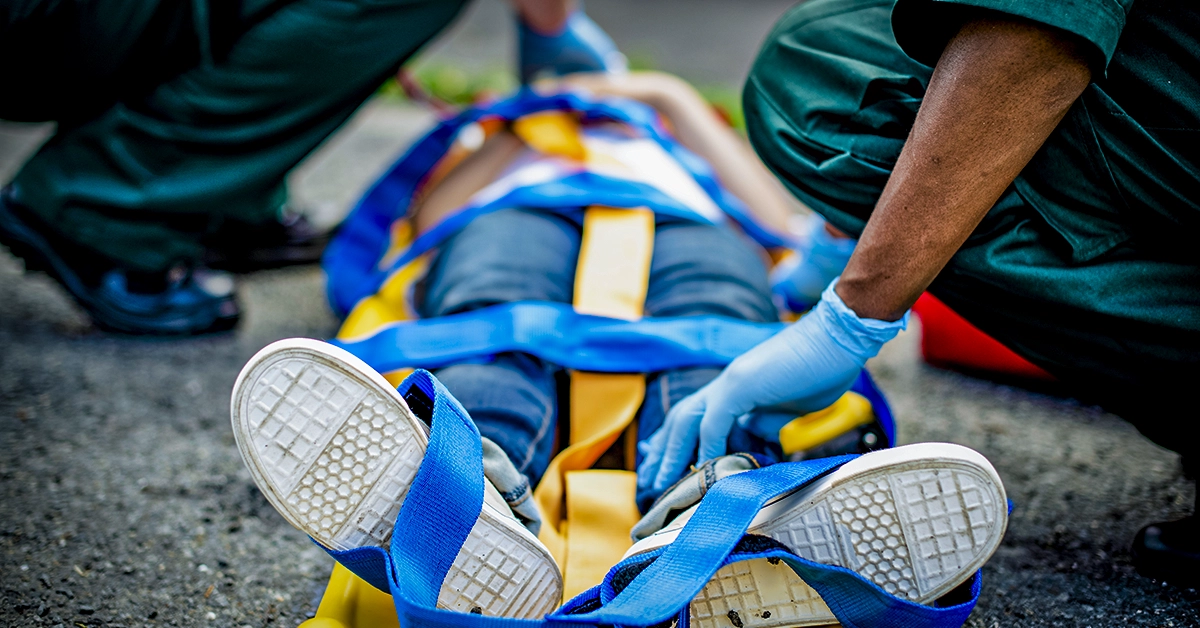 Pessoa sendo colocada em maca por paramédicos, representando a importância de primeiros socorros, como capa do artigo Segurança no Terreiro: Quando a Fé Pede Preparo