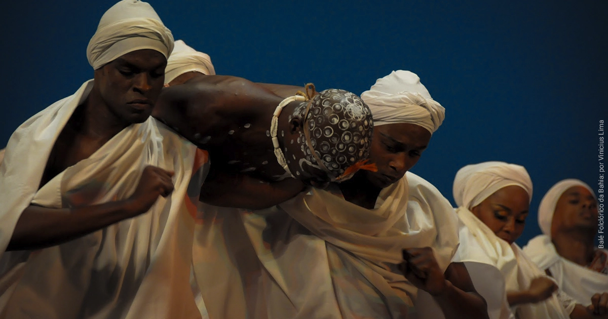 Foto de capa do artigo Guia Seguro para Visitar um Terreiro de Candomblé, dramatizando uma incorporação de Orixá em Iyawo do Candomblé. Créditos da foto para o Balé Folclórico da Bahia, por Vinicius Lima